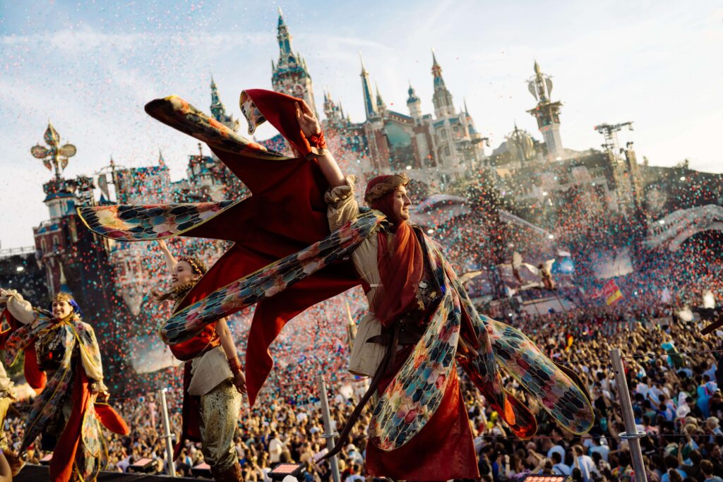 Performers com fantasias coloridas e vibrantes no Tomorrowland Brasil 2024, com um castelo majestoso ao fundo, criando uma atmosfera mágica.