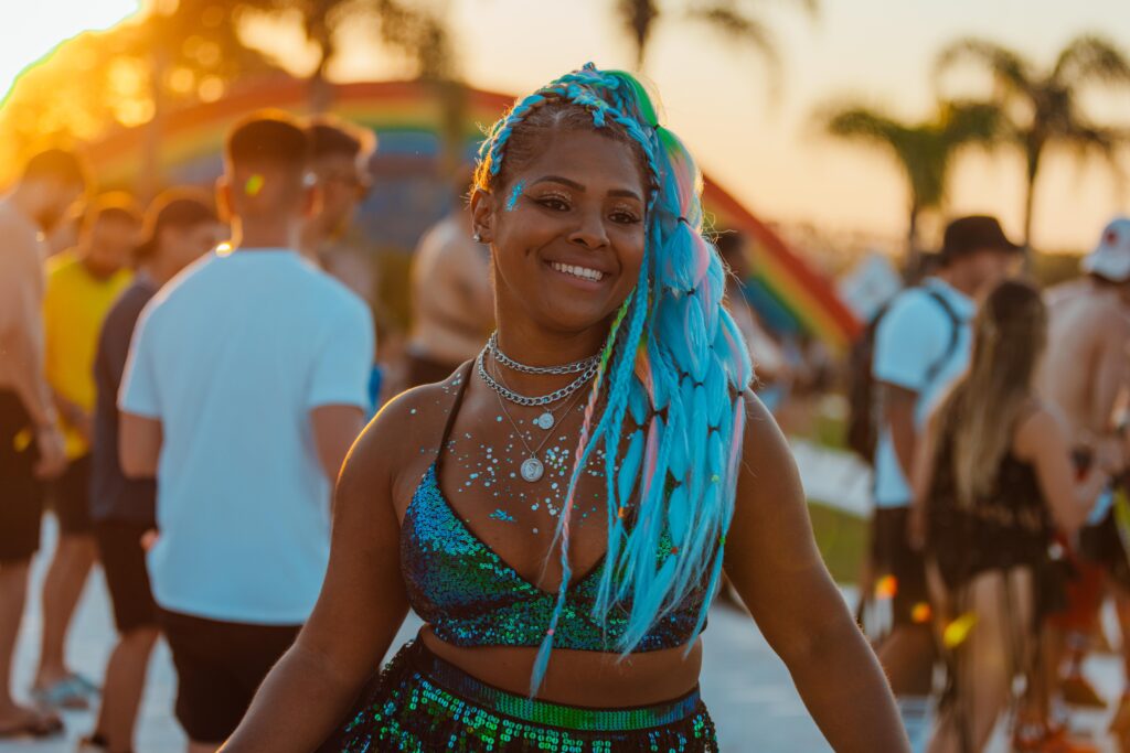 Participante do Tomorrowland Brasil 2024 sorrindo, vestida com roupas e maquiagem de festival, irradiando alegria ao pôr do sol.