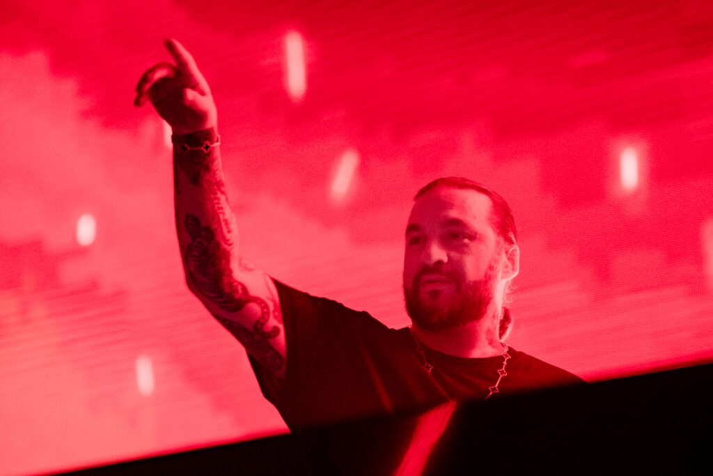 Steve Angello em performance sob luzes vermelhas em um show ao vivo, criando uma atmosfera intensa para o público