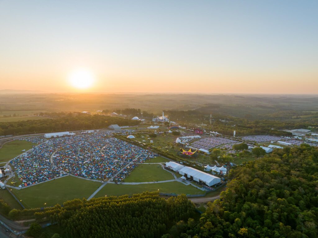 Vista aérea do DreamVille no Tomorrowland Brasil ao amanhecer, mostrando as áreas de camping e o espaço do festival