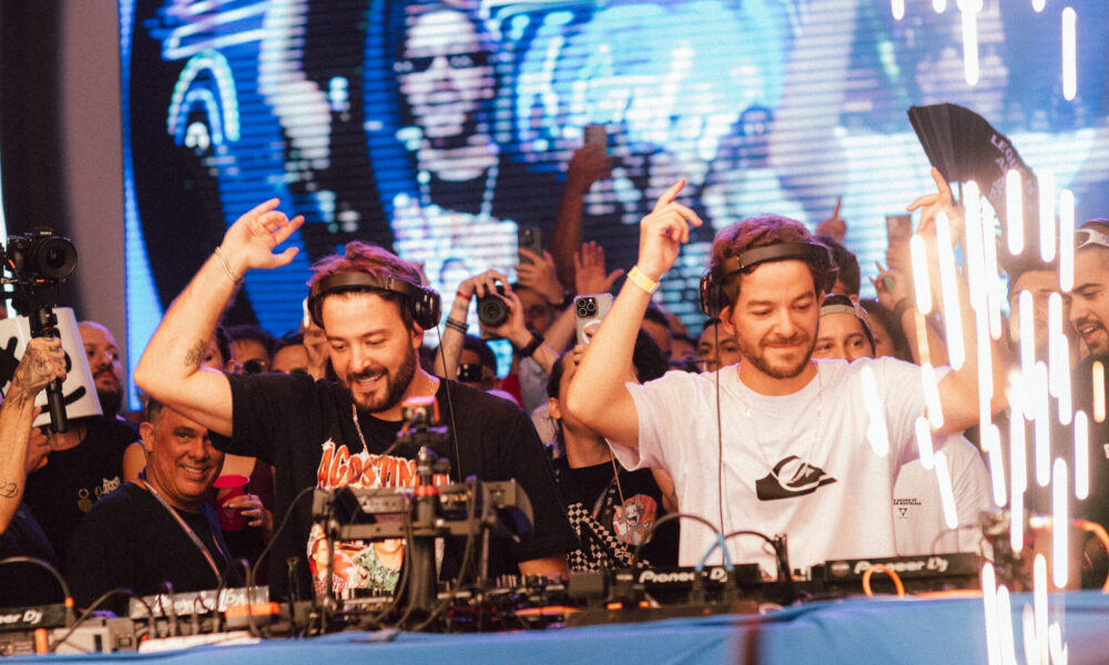 Dupla Dubdogz se apresenta ao vivo em evento no estilo Summer Eletrohits, com público animado e atmosfera nostálgica.