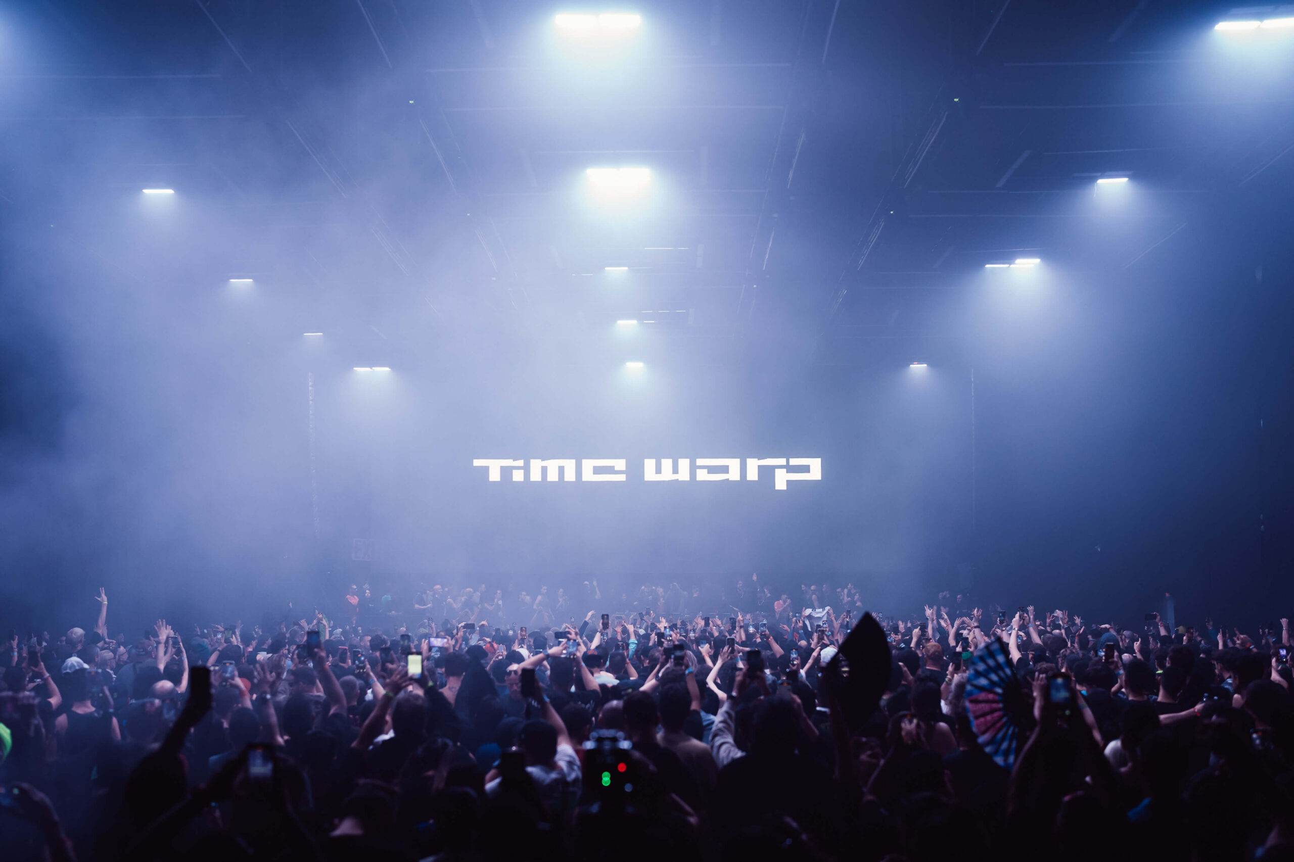 Multidão imersa em luzes e fumaça durante o festival Time Warp 2025 no Brooklyn Storehouse, Nova York