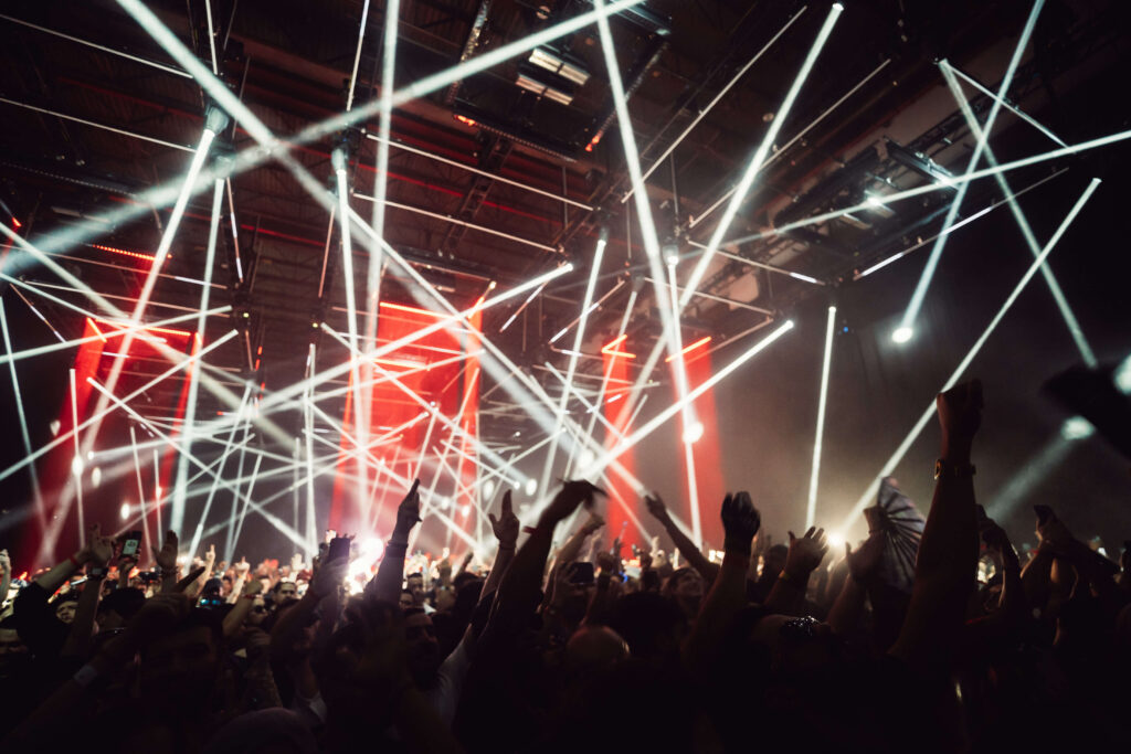 Multidão com braços erguidos sob um show de luzes no festival Time Warp 2025 no Brooklyn Storehouse, em Nova York