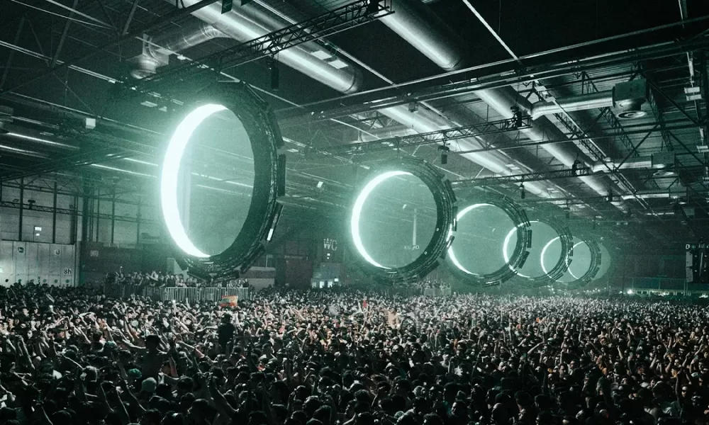 Multidão intensa no Outworld de Klangkuenstler em ambiente industrial, com luzes circulares futuristas e atmosfera de techno cru e imersivo.