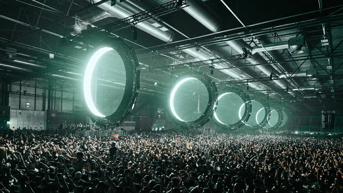 Multidão intensa no Outworld de Klangkuenstler em ambiente industrial, com luzes circulares futuristas e atmosfera de techno cru e imersivo.