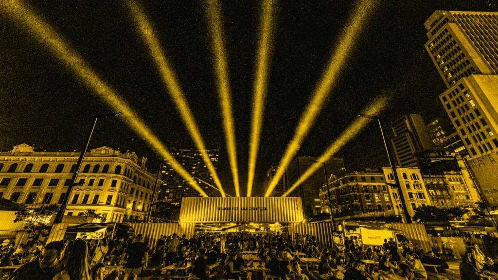 Time Warp Brasil com multidão em festival de techno ao ar livre, iluminação intensa e estética amarela gritty inspirada em pôster underground